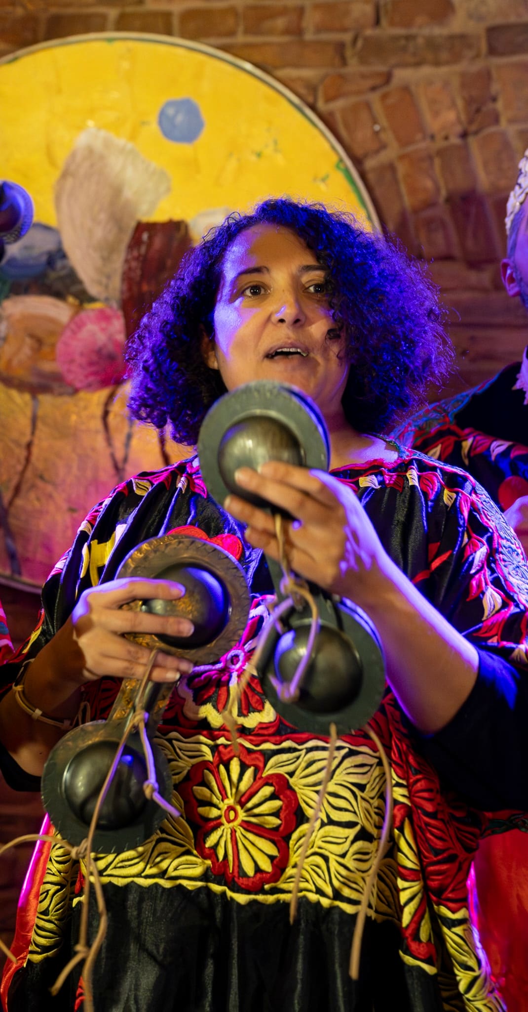 Close-up of a singer playing qraqeb, lit in deep purple against a painted backdrop